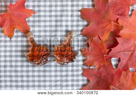 Maple Syrup In A Bottle In A Shape Of Maple Leaf. Red Maple Leaf Background.