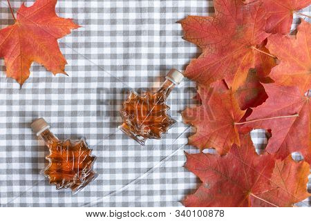 Maple Syrup In A Bottle In A Shape Of Maple Leaf. Red Maple Leaf Background.