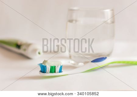 Green Toothbrush With Toothpaste And A Glass Of Water On White Background. Organic Toothcare Concept