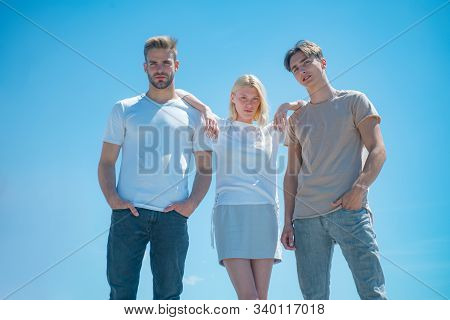 Two Handsome Men And Girl Standing Between Them Look Down At Camera At Clear Blue Sky Background. Co