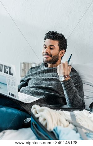 Handsome And Smiling Bi-racial Man In Sweater Reading Newspaper