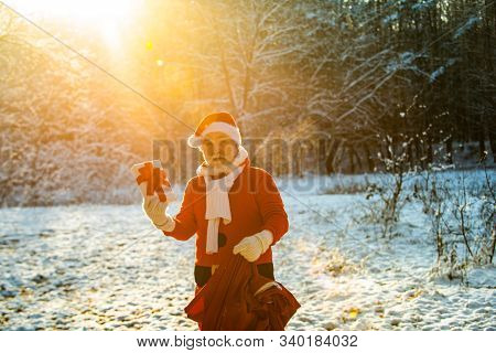 Santa On Christmas Eve Is Carrying Presents To Children In A Red Bag. Santa In The Winter Field. Win