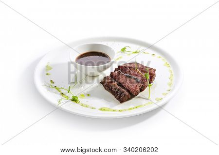 Alternative grilled skirt steak, well done machete fillet on white restaurant plate isolated. Side view of fresh juicy beef grillsteak, barbecue meat with brown spicy sauce and herbs