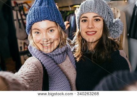 Two Joyful Cheerful Girls Taking A Selfie While Do Shopping At Boutique With Great Choice Of Clothes