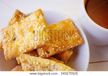 Freshly Prepared Puff Pastry With Sesame Seeds Close-up In A White Plate And A Cup Of Black Tea. Det
