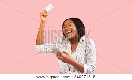 Mobile Banking. Joyful African American Girl Holding Smartphone And Credit Card Dancing Over Pink St