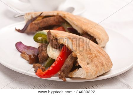 metades de sanduíche de pão pita com carne e legumes em um prato branco