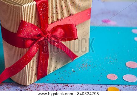 Close Up Of Giftbox Tied With Bright Red Color Ribbon On Purple Background With Sparklets And Confet