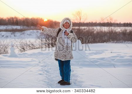 An Elderly Woman Rejoices In The Sun In The Winter Forest. Woman Points Her Hand At The Sun On The W