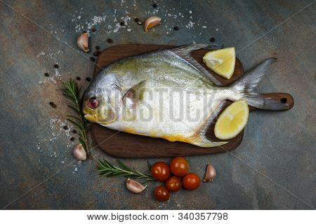 Fresh Pomfret Fish With Herbs Spices Rosemary Tomato And Lemon On Wooden Cutting Board And Black Pla