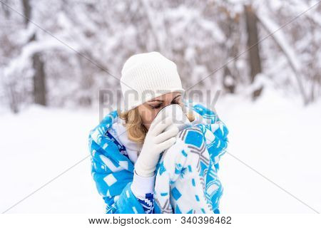 Beautiful Blonde Caucasian Woman In White Khitted Hat And Blue Blanket, Holding A Cup Of Coffee Or T