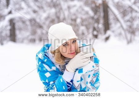 Beautiful Blonde Caucasian Woman In White Khitted Hat And Blue Blanket, Holding A Cup Of Coffee Or T