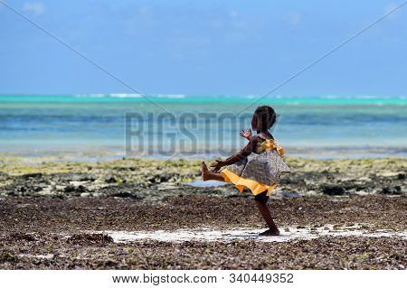 Pingwe, Zanzibar - October 6, 2019: Happy Baby Girl Dancing On Indian Ocean Coast During Low Tide. T