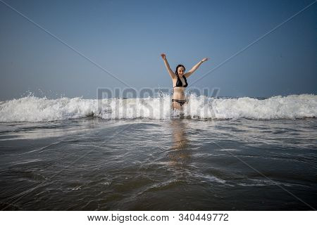 A Young Woman In A Black Swimsuit Spends Time In The Sea Or Ocean. The Girl Takes Refuge From The Wa
