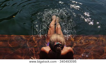 Woman Sit On A Pier In Sunglasses And Swimming Suit. Girl Rest On A Flood Wood Underwater Pier. Lady