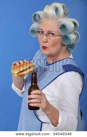 legrační obrázek babičky s natáčky na vlasy vychutnává cheeseburger s pivem