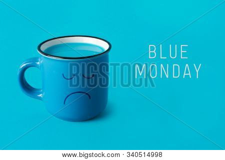 closeup of a blue mug, with a sad face drawn in it, and the text blue monday on a blue background