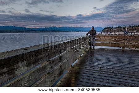 Man Standing On A Pier Looking At Mountains Across A Beautiful Sea