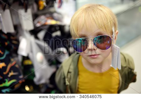 Little Boy Choosing Of Sunglasses In Store. Child Chose Fashionable Glasses And Tries Them On. Prepa