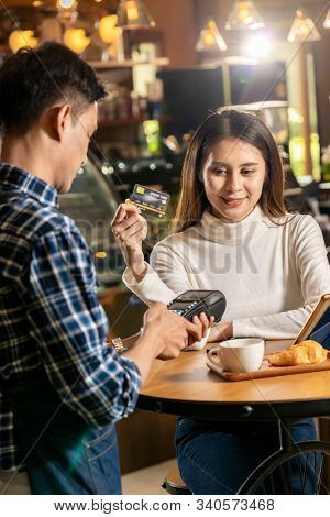 Asian customer using credit card with contactless nfs technology to pay a waiter for coffee purchase at table in cafe.