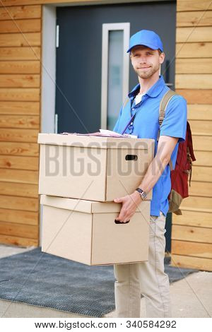 Smiling delivery man in blue uniform delivering parcel box to recipient - courier service concept. Smiling delivery man in blue uniform