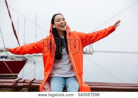 Smiling cheerful attractive young asian woman wearing raincoat spending time outdoors walking at the coastland