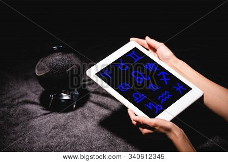 Cropped View Of Astrologer Holding Digital Tablet With Zodiac Signs Near Crystal Ball On Black Velve