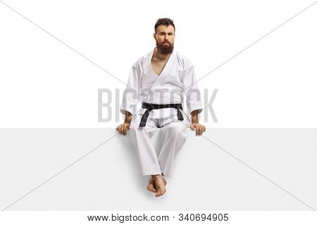 Serious man wearing a karate kimono and sitting on a blank board isolated on white background
