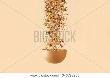 Falling Granola With Candied Fruits And Nuts  To Baige Flying Bowl On Baige Background. Stock Photo 