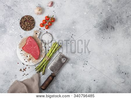 Slice Of Raw Beef Sirlion Steak On Round Chopping Board With Tomatoes,garlic And Asparagus Tips And 