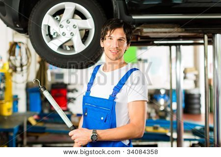 Młody człowiek w niebieskim ogólnej - mechanik - praca z lampą na jacked samochód stacja obsługi
