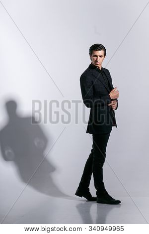 Man In Elegant Suit, Poses With Attitudine, Isoalted On A White Background. Touching His Button On J