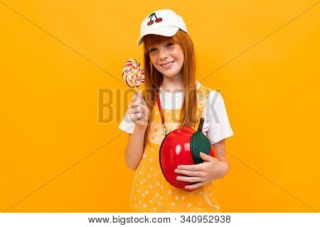 Cacucasian Girl With Red Hair Posing On Camera With Little Apple Bag Isolated On Yellow Background