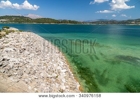 Scenic View At The Gadoura Water Reservoir On Rhodes Island, Greece With Stony Shore, Blue And Turqu