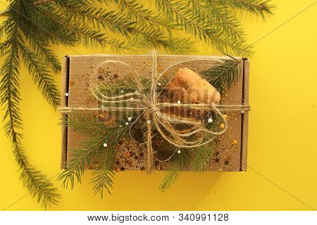 Christmas Present On Yellow Background. Craft Paper Box Decorated With Evergreen Tree, Golden Card A