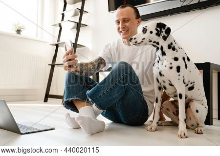 Young happym mid aged man with laptop computer taking a selfie while sitting on a floor with his dog at home
