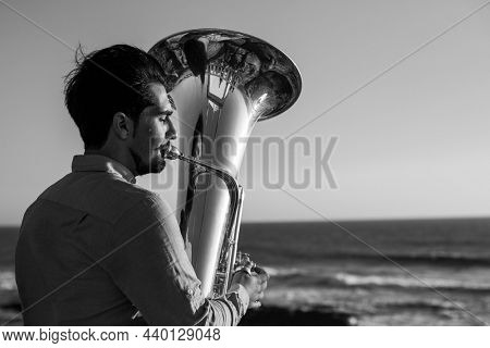 A musician plays a trumpet near the ocean. Black and white photo.