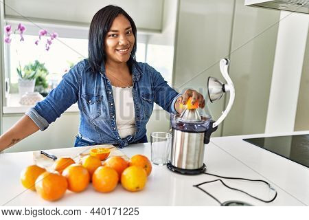 Hispanic brunette woman preparing orange juice at the kitchen