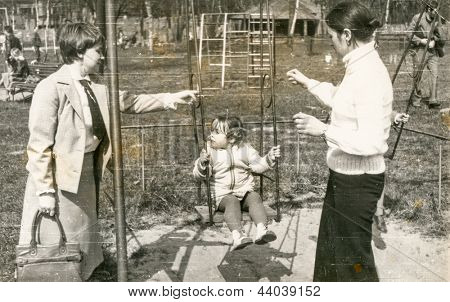 Vintage photo of mother, aunt and daughter on swing (seventies)