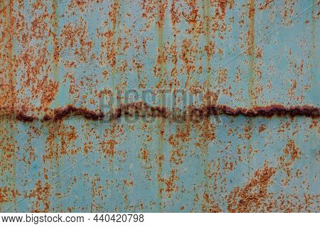 Fragment Of A Green Iron Wall With Foci Of Corrosion. A Strip Of Rusted Metal Is Horizontally Locate