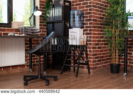Close Up Of Bookshelf And Water Dispenser In Business Office. Empty Desk With Decorations And Waterc