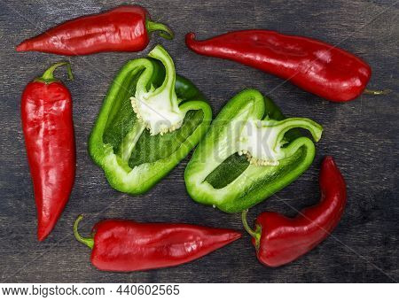 Two Halves Of Fresh Green Bell Pepper Cut Lengthwise Surrounded By Whole Red Pepper Pods On The Dark