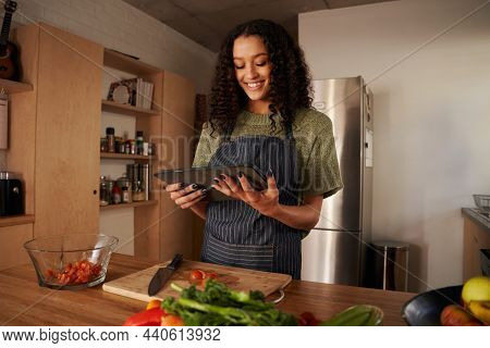 Multi-cultural Young Female Holding Tablet And Reading Recipe While Cooking In Modern Kitchen. Fresh