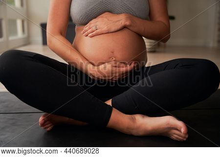Caucasian Female Sitting On Yoga Mat Gently Holding Pregnant Belly