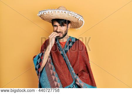 Young hispanic man holding mexican hat looking stressed and nervous with hands on mouth biting nails. anxiety problem. 