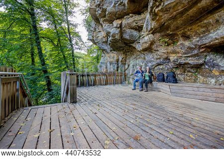 Wooden Platform In A Viewpoint, Bench With Two Hikers Taking A Break With Their Brown Dog, Wall Of A