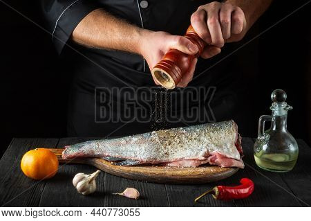 Cook Prepares Fresh Fish Sprinkling Pepper. Preparing To Cook Fish Food. Working Environment In The 