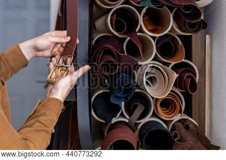 Closeup Hands Of Professional Tanner Choosing Belt Buckle On Wooden Table At Leather Workshop