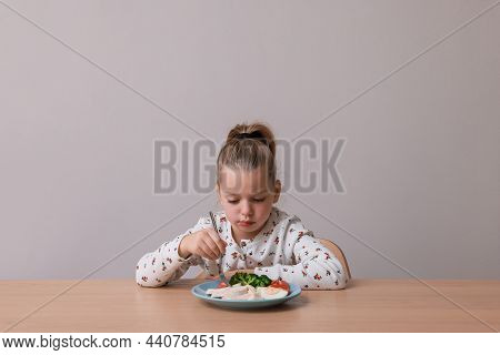 Cute Little Girl Refusing To Eat Her Dinner At Table On Grey Background