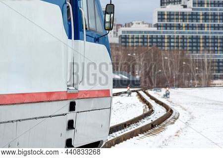 Modern Locomotive On A Narrow Gauge Railway Against The Background Of The City